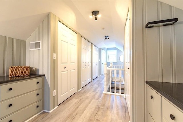 corridor with light wood-type flooring, visible vents, vaulted ceiling, and an upstairs landing