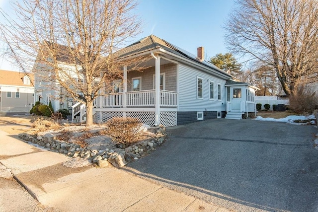 view of front facade featuring entry steps, covered porch, a chimney, and solar panels