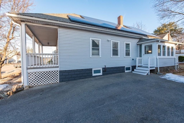 back of house featuring roof with shingles, a chimney, and solar panels