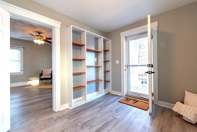 doorway featuring wood finished floors, a ceiling fan, and baseboards