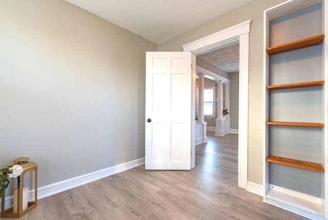 interior space featuring wood finished floors, decorative columns, and baseboards