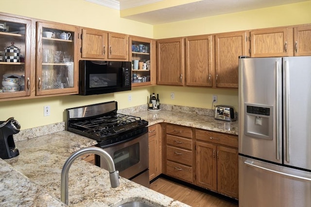 kitchen with brown cabinets, light stone counters, light wood finished floors, glass insert cabinets, and stainless steel appliances