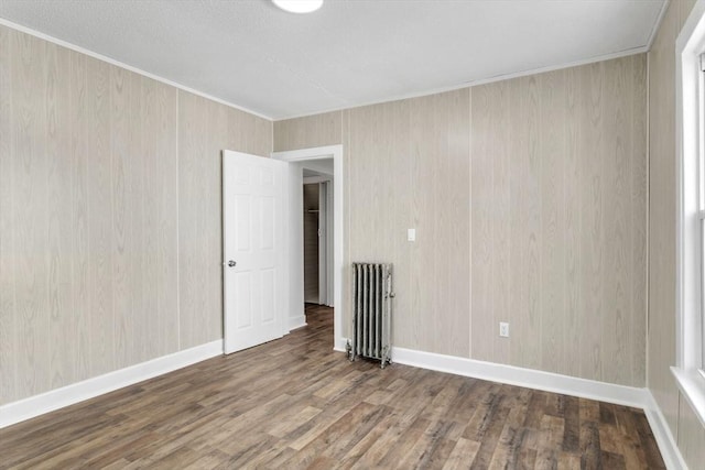 unfurnished room featuring radiator heating unit, baseboards, wood finished floors, and ornamental molding