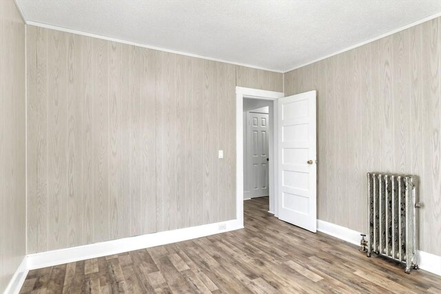 empty room with radiator, baseboards, ornamental molding, and wood finished floors