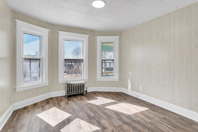 empty room with radiator, baseboards, and wood finished floors