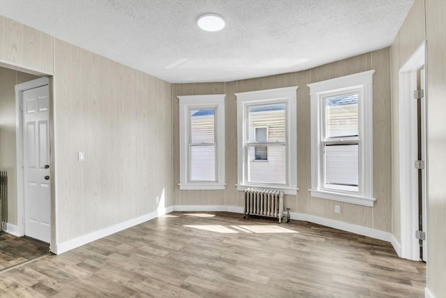 empty room with a textured ceiling, baseboards, wood finished floors, and radiator