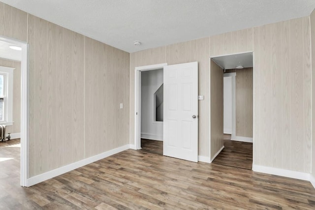 unfurnished bedroom featuring baseboards, a textured ceiling, radiator heating unit, and wood finished floors