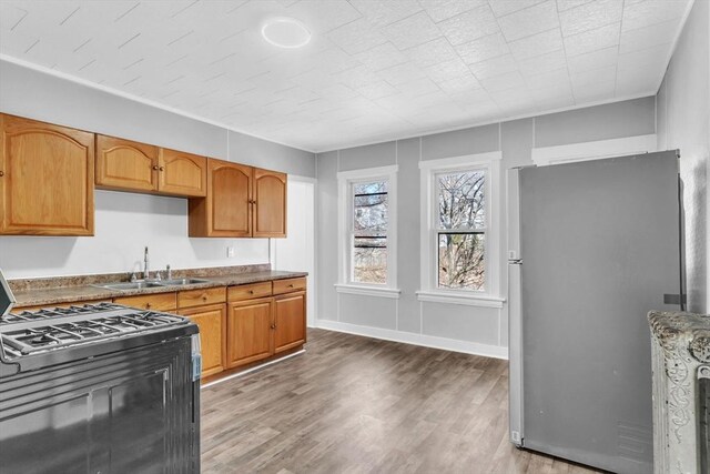 kitchen with baseboards, range with gas stovetop, freestanding refrigerator, light wood-type flooring, and a sink