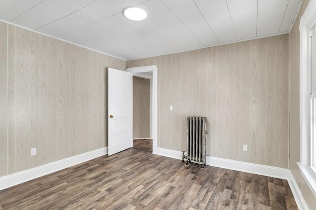 unfurnished room featuring radiator, baseboards, and wood finished floors