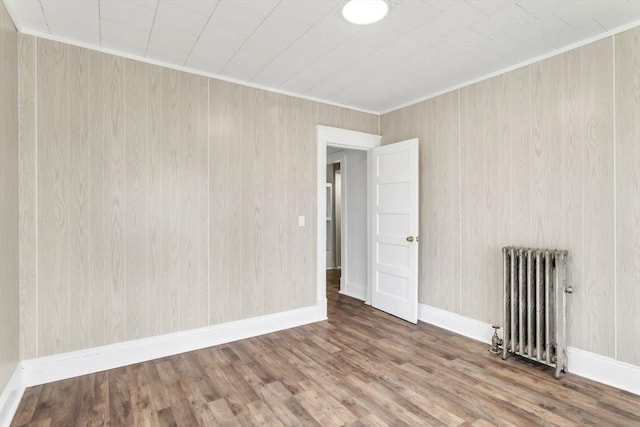 empty room featuring ornamental molding, radiator heating unit, wood finished floors, and baseboards