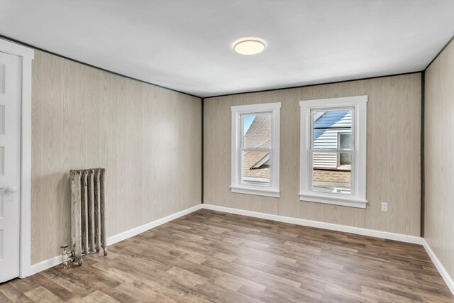 spare room featuring radiator heating unit, baseboards, and wood finished floors