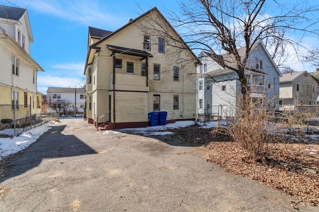 back of property featuring entry steps, aphalt driveway, fence, and a residential view