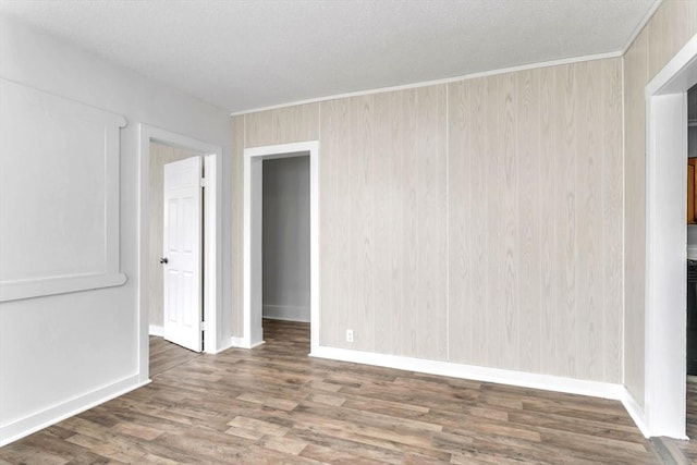 empty room featuring baseboards, a textured ceiling, ornamental molding, and wood finished floors