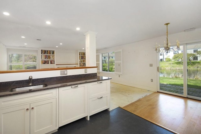 kitchen with a sink, plenty of natural light, an inviting chandelier, and dark stone countertops