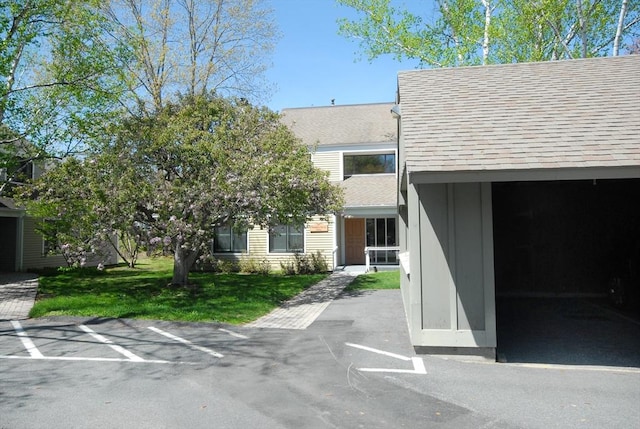 view of front of home featuring roof with shingles, uncovered parking, and a front yard