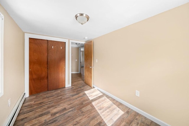 unfurnished bedroom featuring a closet, baseboard heating, dark wood finished floors, and baseboards