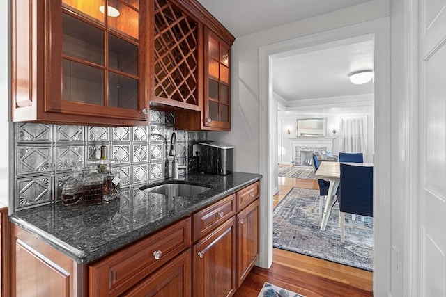 kitchen with dark stone countertops, wood finished floors, a fireplace, a sink, and tasteful backsplash