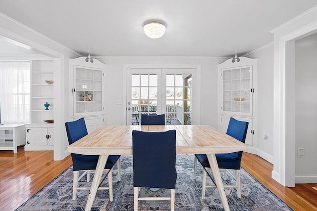 dining area with french doors, light wood-type flooring, crown molding, and baseboards