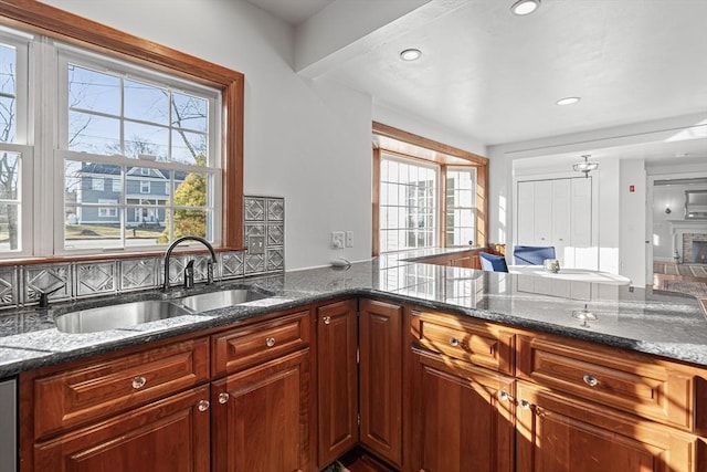 kitchen with a sink, dark stone counters, a brick fireplace, and decorative backsplash