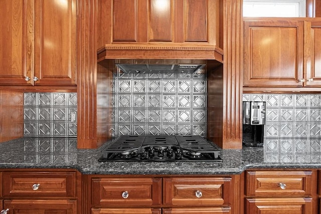 kitchen featuring backsplash, dark stone counters, black gas stovetop, and brown cabinets