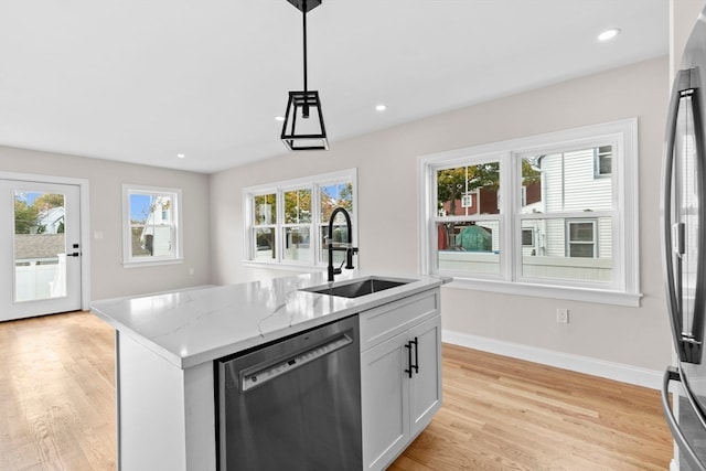 kitchen with light stone countertops, sink, stainless steel appliances, pendant lighting, and a center island with sink