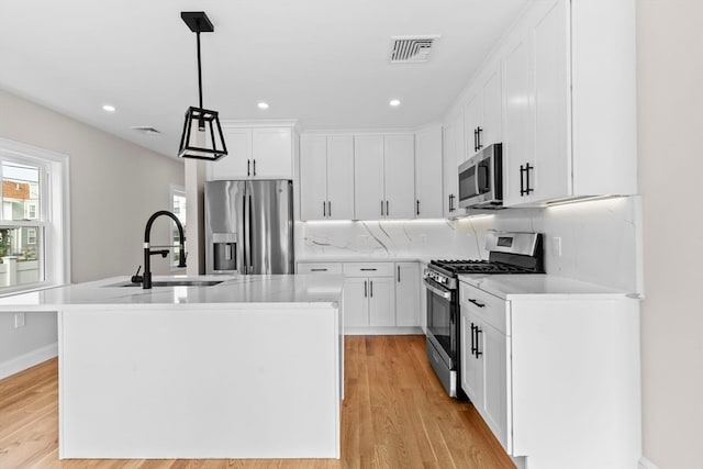 kitchen featuring hanging light fixtures, appliances with stainless steel finishes, white cabinetry, a kitchen island with sink, and sink