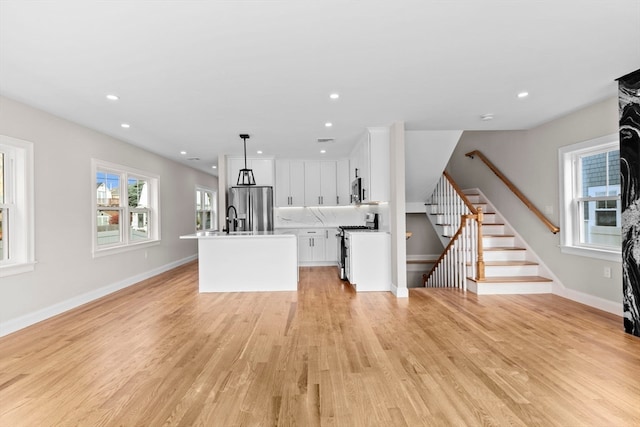 kitchen with appliances with stainless steel finishes, a kitchen island with sink, hanging light fixtures, and light hardwood / wood-style floors