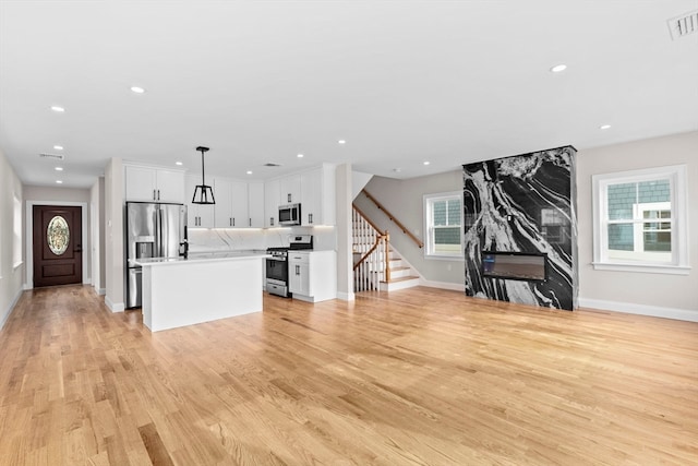 kitchen with a healthy amount of sunlight, appliances with stainless steel finishes, hanging light fixtures, and white cabinets