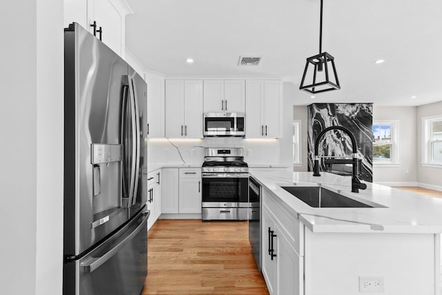 kitchen with white cabinets, hanging light fixtures, appliances with stainless steel finishes, light stone countertops, and light wood-type flooring