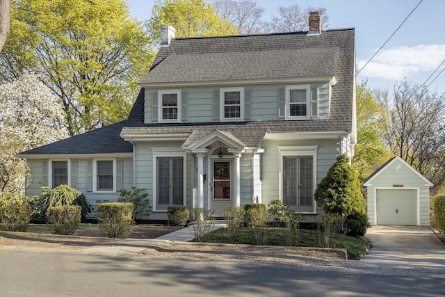 view of front of home with driveway, a chimney, roof with shingles, a detached garage, and an outdoor structure