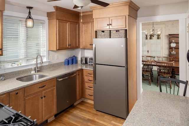 kitchen featuring light wood-style floors, a sink, ceiling fan with notable chandelier, hanging light fixtures, and stainless steel appliances