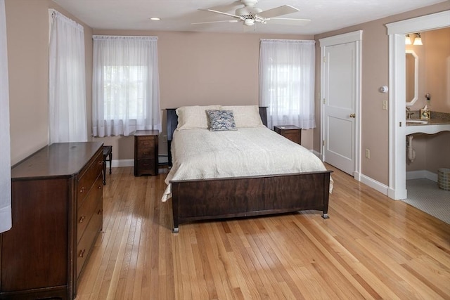 bedroom featuring ceiling fan, a sink, baseboard heating, light wood finished floors, and baseboards