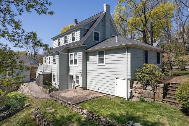 back of house featuring a lawn, a shingled roof, a patio area, and a chimney