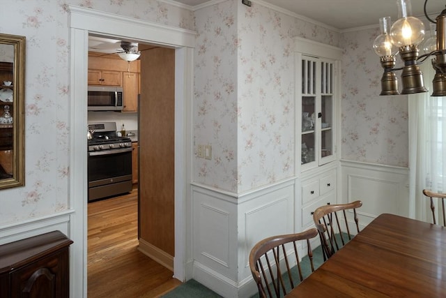 dining area with a ceiling fan, ornamental molding, wood finished floors, and a wainscoted wall