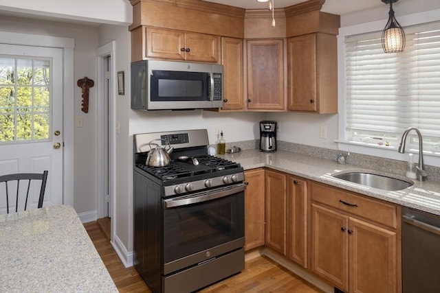 kitchen with appliances with stainless steel finishes, brown cabinets, light wood-type flooring, a sink, and light stone counters