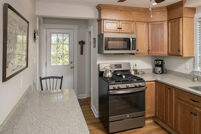 kitchen with ceiling fan, brown cabinets, a sink, light wood finished floors, and appliances with stainless steel finishes