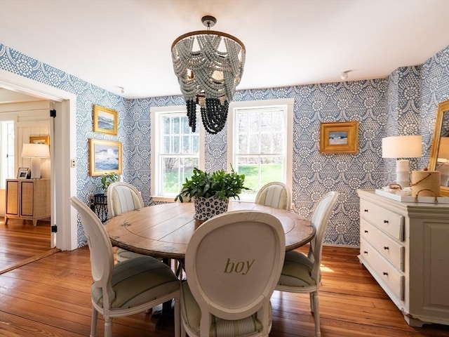 dining space with an inviting chandelier, wallpapered walls, and light wood-style flooring