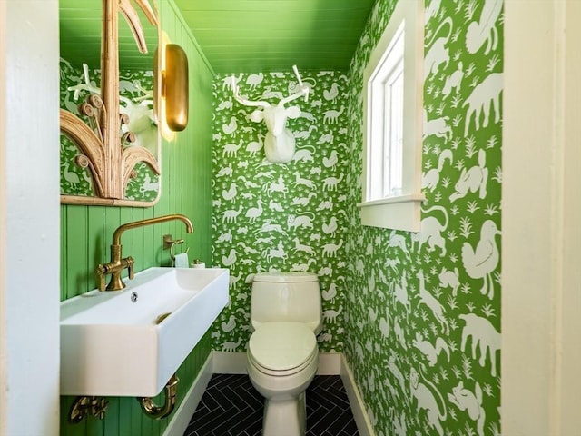 bathroom featuring toilet, baseboards, wallpapered walls, tile patterned floors, and a sink