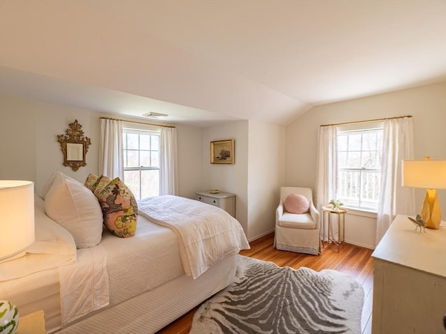 bedroom with light wood-style floors, baseboards, vaulted ceiling, and visible vents
