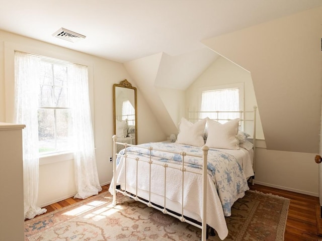 bedroom with baseboards, visible vents, wood finished floors, and lofted ceiling