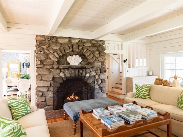 living room featuring a stone fireplace, beam ceiling, stairway, and wood finished floors