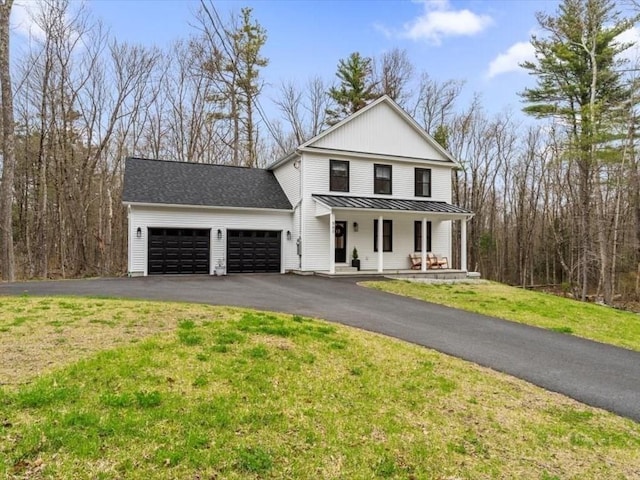 view of front of home featuring an attached garage, a front lawn, a standing seam roof, covered porch, and driveway
