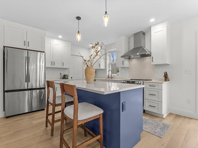 kitchen with wall chimney range hood, stainless steel fridge, a center island, white cabinets, and light wood finished floors