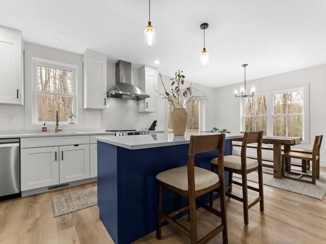 kitchen with wall chimney range hood, dishwasher, a sink, light wood finished floors, and a breakfast bar