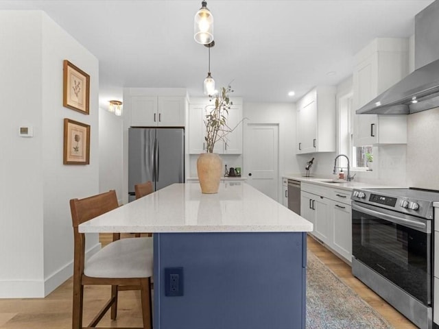kitchen with wall chimney range hood, appliances with stainless steel finishes, a sink, a kitchen breakfast bar, and light wood-type flooring