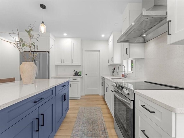 kitchen with white cabinets, appliances with stainless steel finishes, a sink, light wood-style floors, and wall chimney exhaust hood