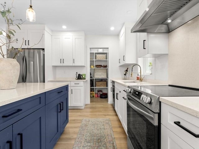 kitchen with appliances with stainless steel finishes, range hood, a sink, light wood finished floors, and white cabinetry