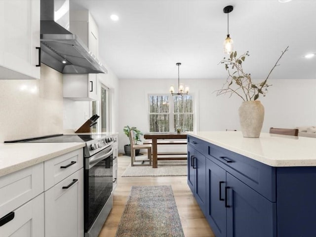 kitchen with stainless steel electric stove, white cabinets, wall chimney exhaust hood, and a chandelier