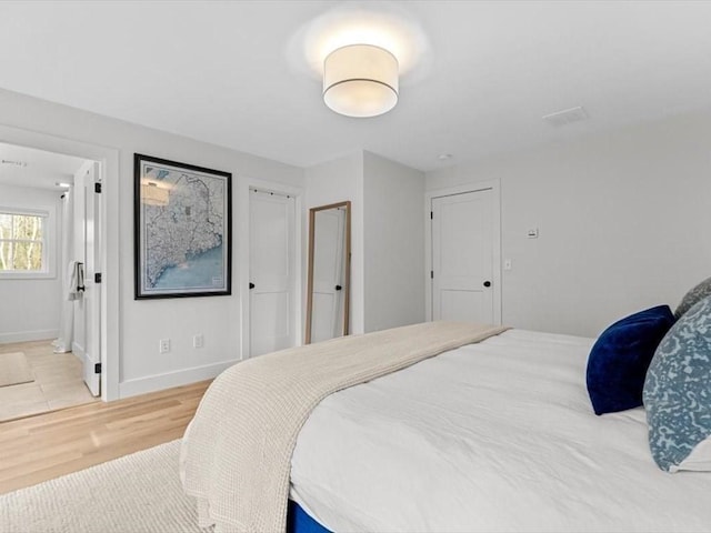 bedroom featuring baseboards, light wood-style flooring, and ensuite bath