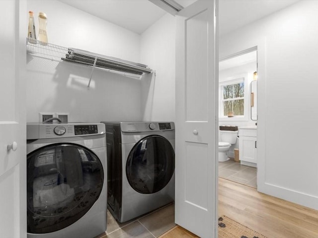 clothes washing area featuring washing machine and clothes dryer, laundry area, and light wood-style flooring